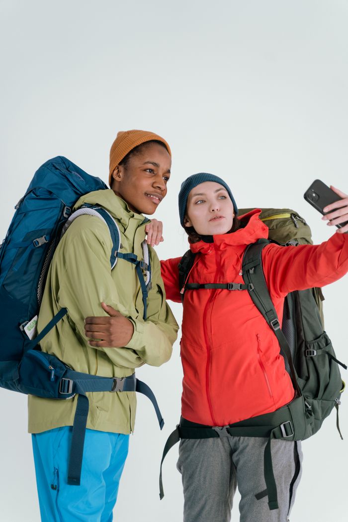 trusted-partner Two diverse hikers take a selfie in a studio setting, capturing their travel adventure.